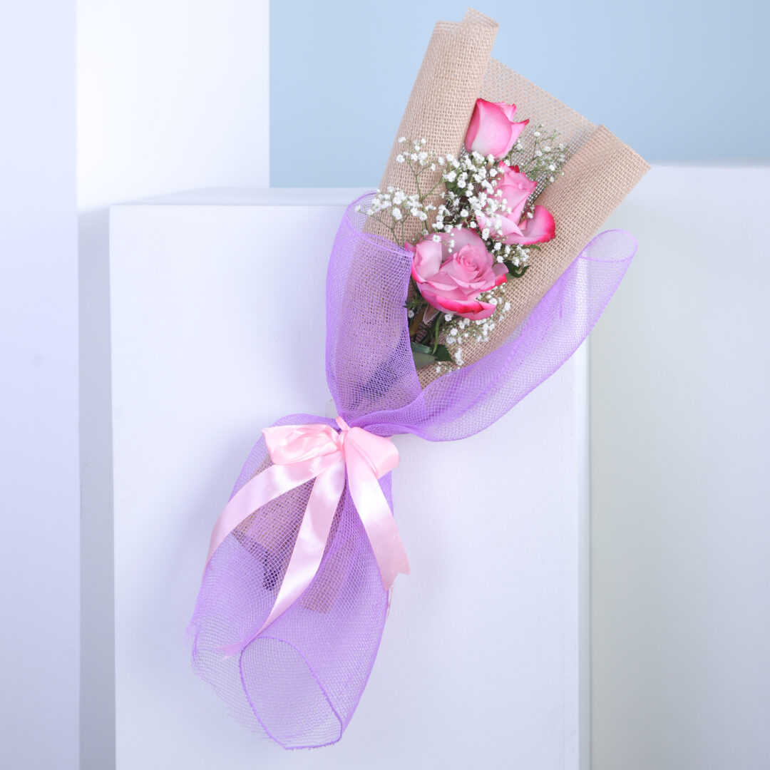 A bouquet of pink roses with a purple ribbon.